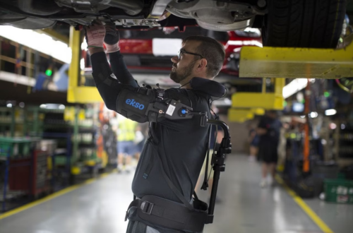 Ouvrier sur chaîne d'assemblage Ford portant l'exosquelette EksoVest pour le travail bras levés