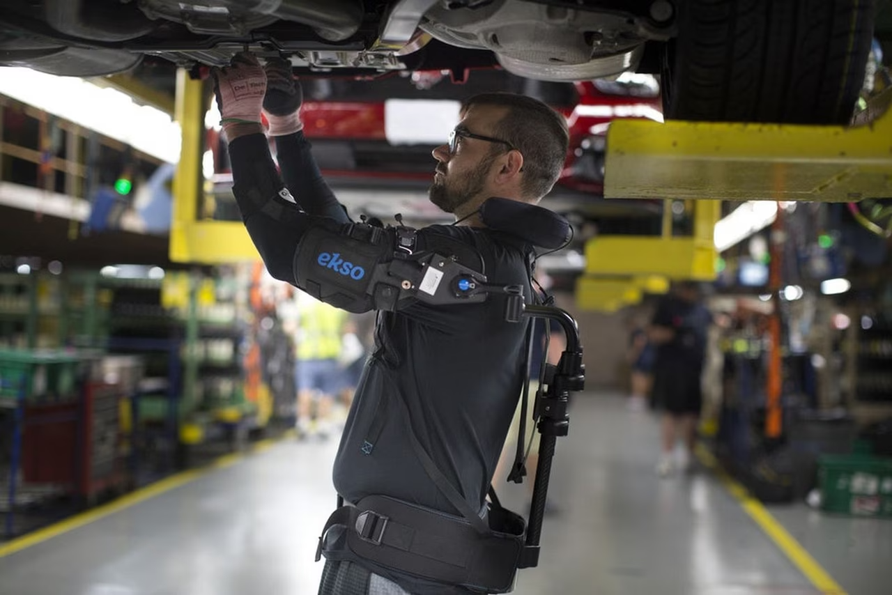 Ouvrier sur chaîne d'assemblage Ford portant l'exosquelette EksoVest pour le travail bras levés
